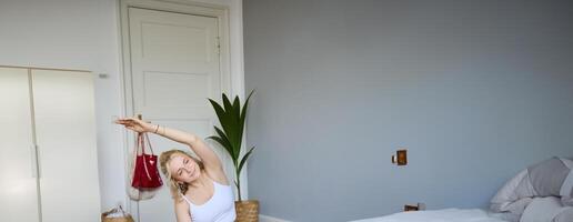 Portrait of young blogger, yoga content creator, showing exercises, recording of herself working out at home on rubber mat photo