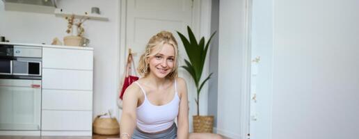 Vertical shot of woman recording her workout on digital camera, making a about yoga and fitness at home, sitting on rubber mat in activewear photo