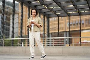 retrato de asiático hembra modelo con teléfono. joven coreano niña participación teléfono inteligente en calle, utilizando teléfono foto