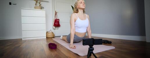 Portrait of young blogger, yoga content creator, showing exercises, recording of herself working out at home on rubber mat photo