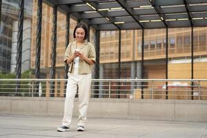 retrato de asiático hembra modelo con teléfono. joven coreano niña participación teléfono inteligente en calle, utilizando teléfono foto