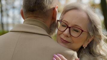 Close up female face and male back retired couple embracing hugging in city autumn park outdoors mature 60s woman hug man closeness tender relationships affectionate love support romance at old age video