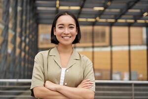 People. Portrait of confident korean girl, young student cross arms on chest, standing in power pose and smiling at camera photo