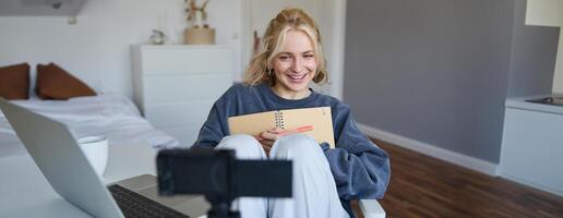 Portrait of cute, smiling young social media content creator, girl records on digital camera and stabiliser, holds notebook, talks to audience, vlogging in her room photo