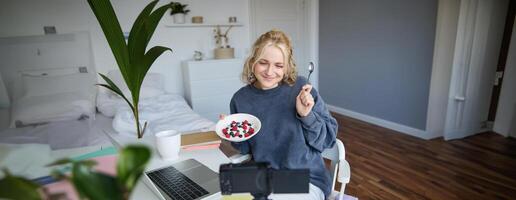 Portrait of young woman vlogger, recording herself while eating homemade healthy breakfast, creating vlog content for followers photo
