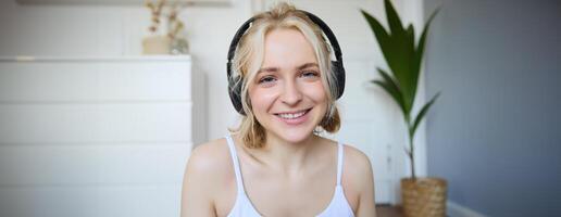 Concept of people and lifestyle, Close up of beautiful blond woman in wireless headphones, listens to music, enjoys good quality sound in new earphones photo