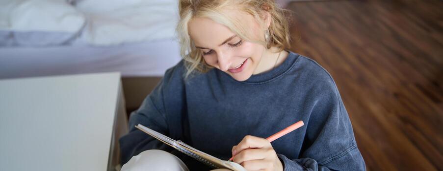 Close up portrait of smiling girl, writing in notebook, adds notes to her diary, smiling while doing homework photo