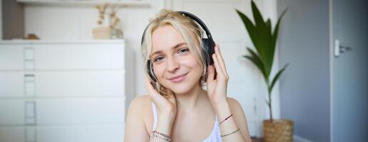 Concept of people and lifestyle, Close up of beautiful blond woman in wireless headphones, listens to music, enjoys good quality sound in new earphones photo