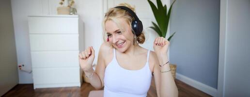 Portrait of beautiful blond girl, fitness woman dancing in wireless headphones, enjoying working out tuning into favourite song photo