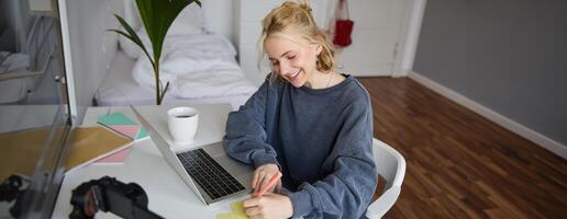 retrato de joven mujer distancia aprendiendo, trabajando desde hogar con computadora portátil, haciendo notas, estudiante estudiando en remoto, haciendo en línea curso foto