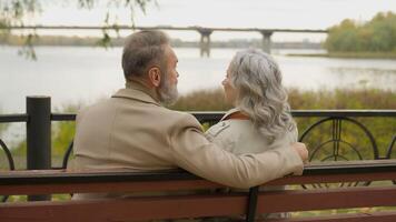 Rear back view happy senior couple family sit on bench love retirement mature woman man enjoy romantic date in city park middle aged Caucasian male and female grandparents talk relax together outdoors video