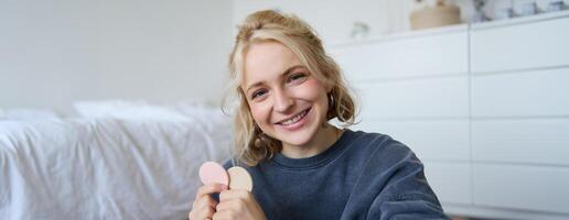 Close up portrait of happy, beautiful young vlogger, content maker recording about makeup, showing beauty products on camera, smiling happily photo