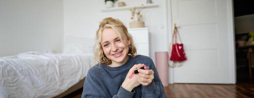 Portrait of beautiful young woman, content creator for social media, sitting in front of digital camera, recording about makeup, showing lipstick swatches on her skin photo