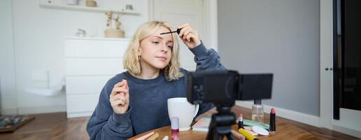 Portrait of blond smiling woman records a lifestyle blog, vlogger or makeup artist recording for social media, holding mascara, reviewing beauty products for followers online photo