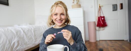 Lifestyle, beauty blogger, woman recording of her putting on makeup, talking to camera, making online tutorial, showing her lip gloss or lipstick to followers, sitting on floor with cup of tea photo