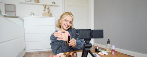 Portrait of young content maker, woman blogger recording a on digital camera, showing lipstick colour to her followers, creating lifestyle vlog for social media account photo