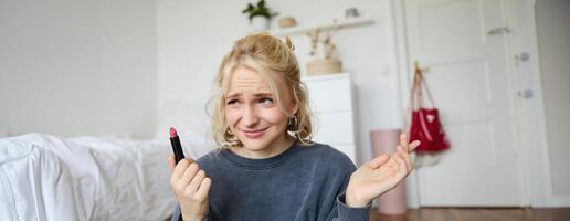 Portrait of woman, vlogger looking disappointed, showing lipstick and shrugging shoulders, recording about makeup for social media account photo