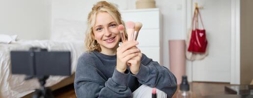 Portrait of content media creator, blogger sits in her room and records of her favourite makeup brushes, talks on camera photo