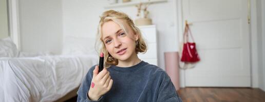 retrato de hermosa joven mujer, contenido creador para social medios de comunicación, sentado en frente de digital cámara, grabación acerca de constituir, demostración lápiz labial muestras en su piel foto