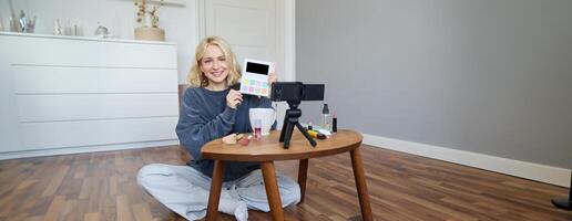 Portrait of beautiful smiling woman, recording in her room, has camera on coffee table, reviewing makeup, doing lifestyle vlog for social media account, records a tutorial photo