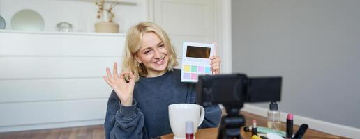 Portrait of beautiful smiling woman, recording in her room, has camera on coffee table, reviewing makeup, doing lifestyle vlog for social media account, records a tutorial photo