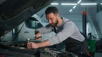 caucasien homme technicien ouvrier dépanneur mécanicien vérifier réparer problème en dessous de ouvert voiture capuche souriant content Masculin gars dans uniforme utilisation clé clé instrument réparation voiture dans garage auto un service station video