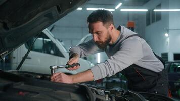 caucasiano homem cansado Exausta auto mecânico excesso de trabalho consertando motor dentro aberto carro de capuz reparação veículo com chave inglesa ferramenta às garagem fixação quebrado automóvel Verifica manutenção dentro serviço estação video