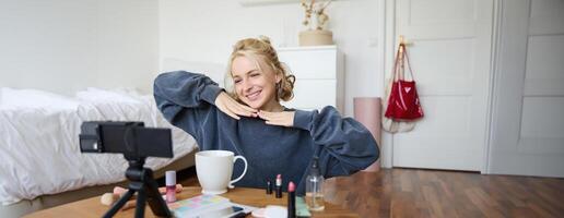 Lifestyle blogger records of herself while doing hairstyle, showing makeup lifehacks for social media followers, vlogging, using camera for her blog, sitting in a room, drinking tea photo