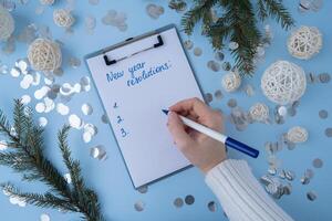 Female hands writing handwritten new year resolutions aims goals on paper notepad. Preparation for New Year. Concept of planning and setting goals for personal development photo