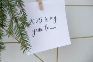 2025 IS MY YEAR TO text on white paper note on vision board with Christmas decor. New year aims resolutions. New me you concept visualizing dreams photo