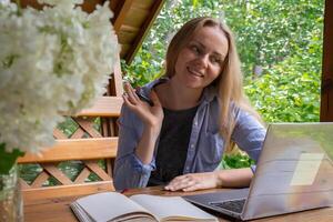 Young woman freelancer working online using laptop and enjoying the beautiful nature outdoors in garden. Online meeting education. Worcation, work from vacation, hybrid work model photo