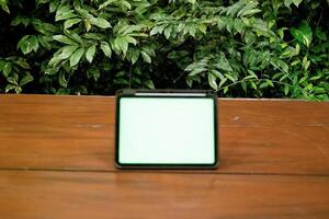 difuminar verde pantalla ipad o tableta en de madera mesa con verde plantas antecedentes foto