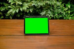 Green Screen iPad or Tablet on Wooden Table with Green Plants Background photo