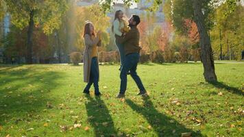 caucásico contento familia fin de semana fiesta naturaleza al aire libre en ciudad otoño parque juntos amoroso padre levantar pequeño niño niño niña hija girar torneado giro girar alrededor jugar divertido juego madre aplaudiendo video