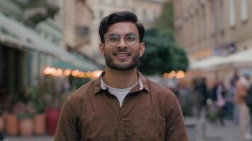 Portrait handsome young gen z Indian Arabian ethnic man guy male happy successful businessman model smiling student client looking camera cheerful smile business outside evening city street cafeteria video