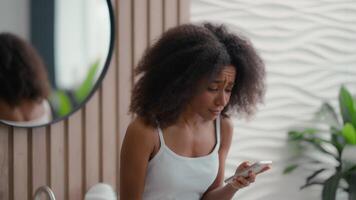 africano americano bellissimo donna a mattina bagno quotidiano bellezza pelle capelli cura femmina emotivo frustrato triste irritato preoccupazione ragazza leggere cattivo notizia mobile Telefono problema fallimento terribile sms smartphone video