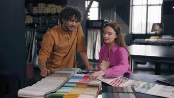 Multiracial couple buyers choosing fabric samples collection buying cloth in atelier Arabian Indian man salesman fashion designer consult Caucasian woman customer discuss choose materials house design video