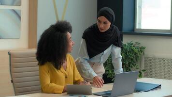 diverso negocio mujer multirracial hembra mujer de negocios trabajando juntos a oficina islámico musulmán en hijab jefe mentor líder ayuda africano americano trabajador ordenador portátil en línea proyecto enseñar interno explique video