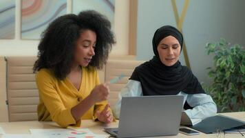 Multiethnic women girls working with laptop computer at office diverse female businesswomen African American mentor help intern teach muslim employee in hijab two business colleagues online studying video