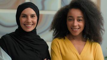 Corporate portrait two multiracial women happy joyful smiling diverse multiethnic businesswomen African American female and Arabian muslim islamic girl in hijab business partners colleagues at office video