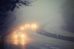 carros en el niebla. malo invierno clima y peligroso automóvil tráfico en el la carretera. ligero vehículos en niebla. foto