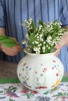 Female put bouquet of lilies of valley in vase photo