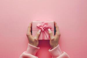 Woman in pink sweater holding in hands one pink gift boxes on pink background. Present for Mothers day, Valentines, Birthday, 8 March. Shopping Sale concept. photo