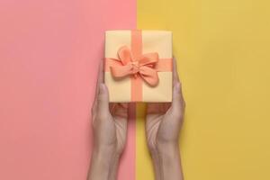 Women's hands holding one yellow present box on pink yellow background divided in center. Gift for Mother's day, Birthday, 8 March. Shopping Sale concept. photo