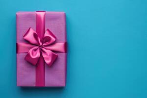 Big present box wrapped in fuchsia color shiny paper with ribbon bow on it. Vivid blue background with place for text on right side. Happy Holidays or Shopping Sale. photo