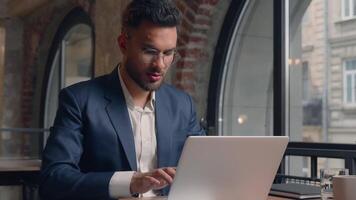 Indian male businessman guy manager freelancer at office finish project end working day accomplish close laptop free happy relaxed business man put hands behind head lean on chair relax cheerful smile video