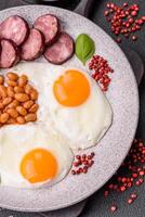 English breakfast with fried eggs, bacon, beans, tomatoes, spices and herbs photo