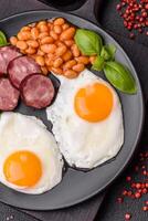 English breakfast with fried eggs, bacon, beans, tomatoes, spices and herbs photo