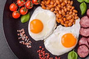 English breakfast with fried eggs, bacon, beans, tomatoes, spices and herbs photo