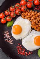 English breakfast with fried eggs, bacon, beans, tomatoes, spices and herbs photo